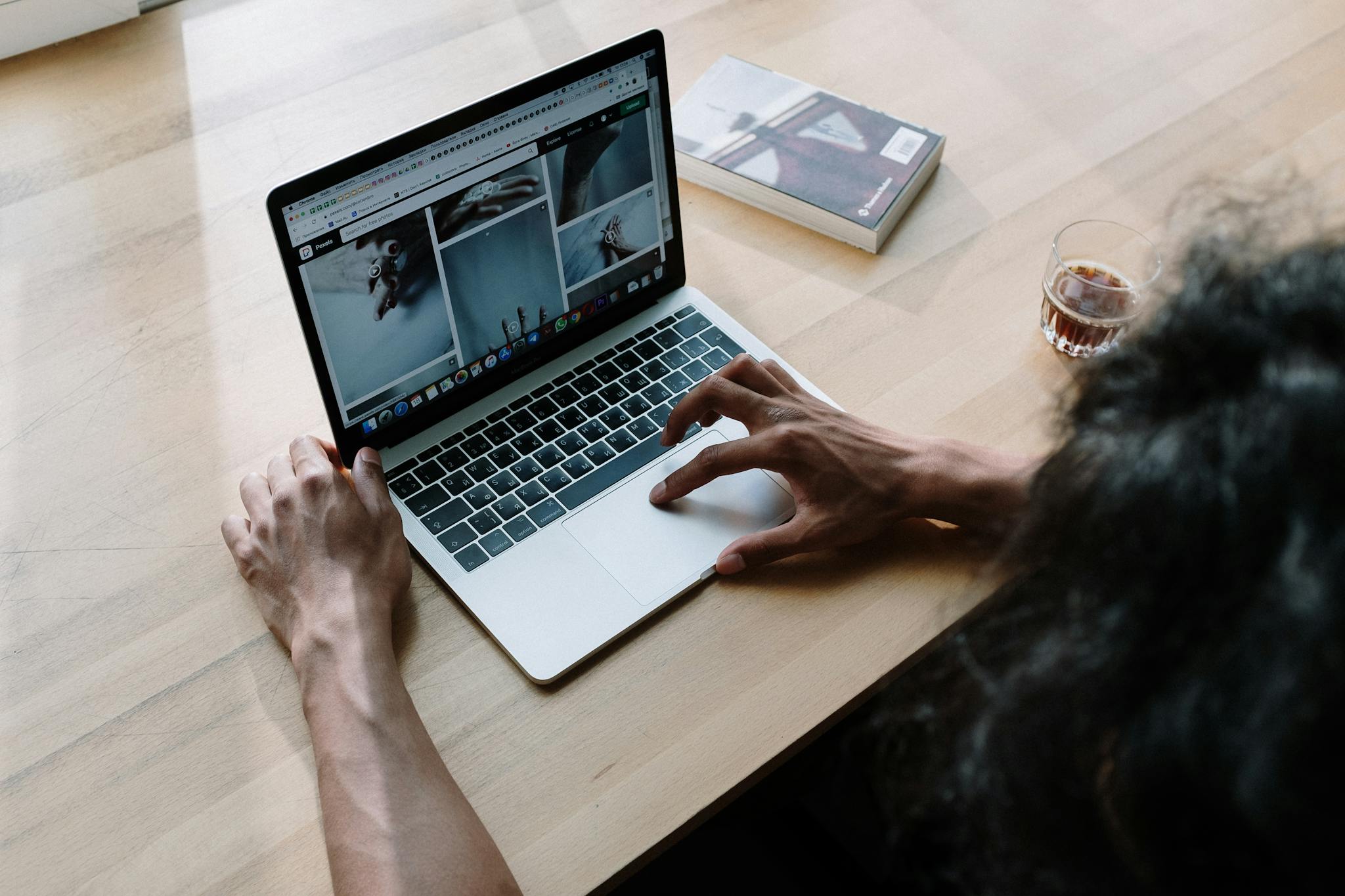 A person browsing images on a laptop with coffee on a wooden table, creating a relaxed workspace vibe.