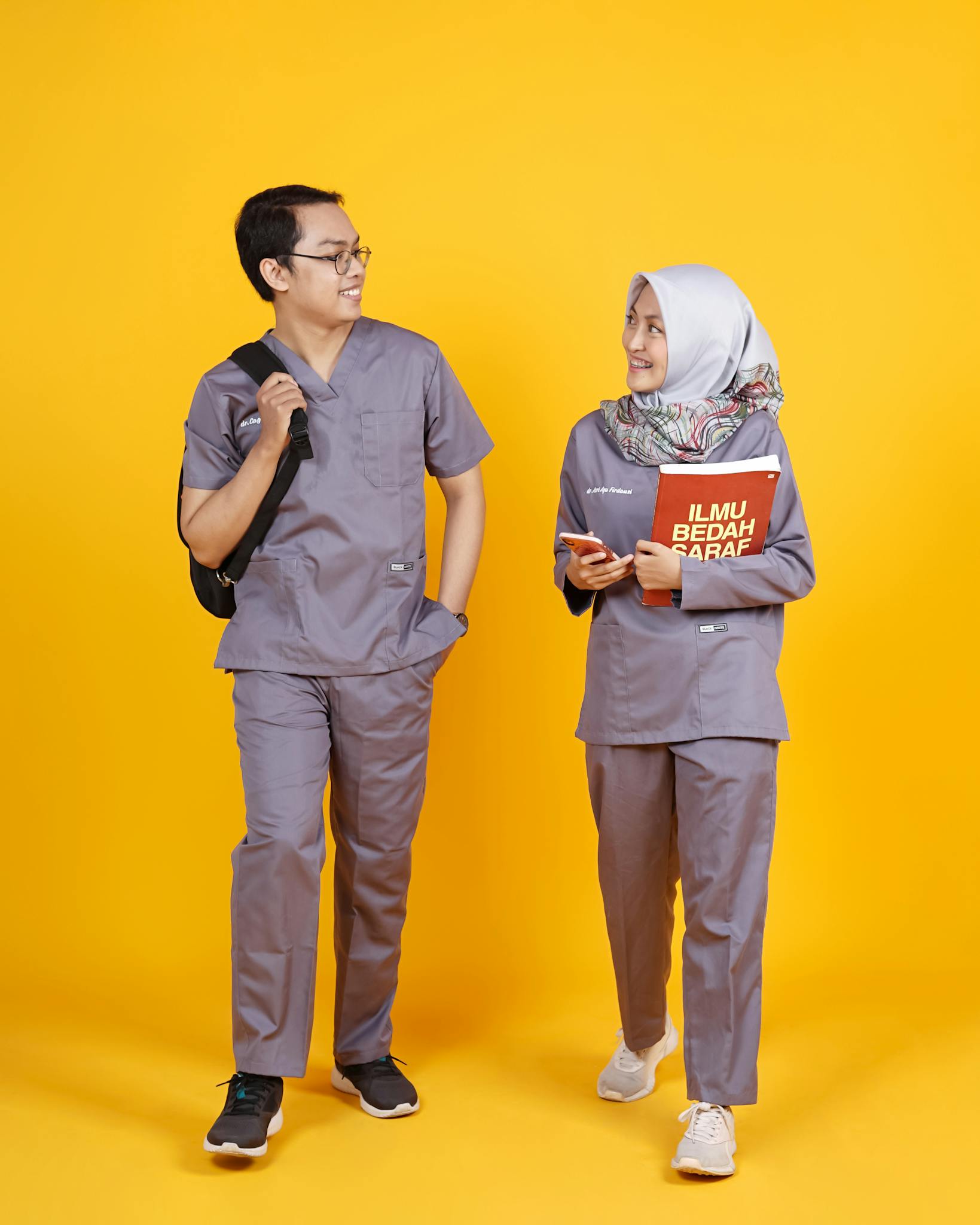 Two healthcare professionals in gray scrubs smiling and conversing.